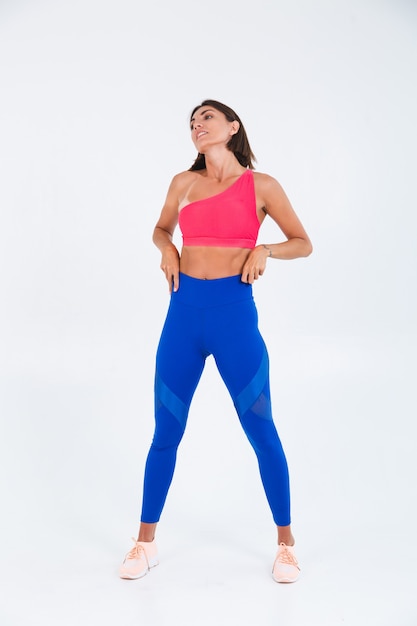Fit gebräunte sportliche Frau mit Bauchmuskeln, Fitnesskurven, trägt Top und blaue Leggings auf weiß