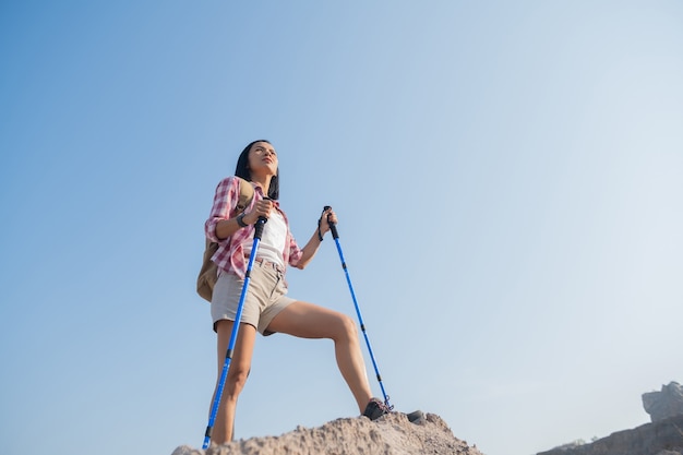 fit junge Frau, die in den Bergen steht, die auf einem felsigen Gipfelgrat mit Rucksack und Stange stehen, die über Landschaft schauen.