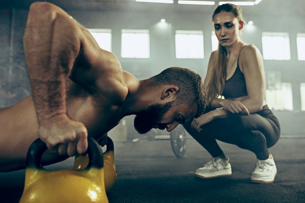 Fit junger Mann, der Hanteln hebt, die in einem Fitnessstudio trainieren