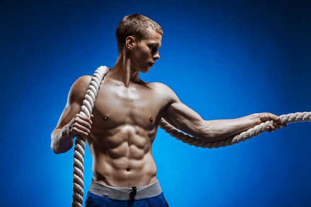 Fit junger Mann mit schönen Torso und einem Seil an der blauen Wand