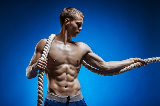 Fit junger Mann mit schönen Torso und einem Seil an der blauen Wand