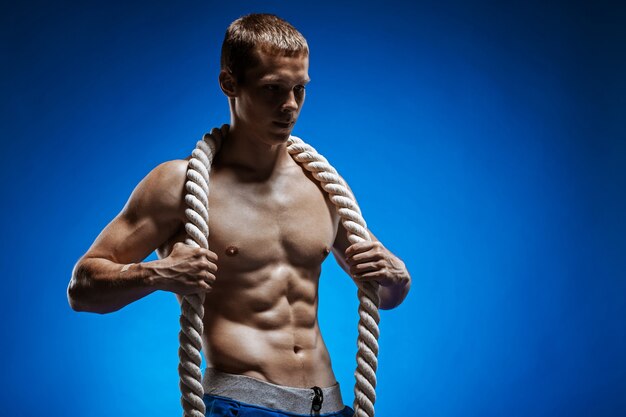 Fit junger Mann mit schönen Torso und einem Seil an der blauen Wand