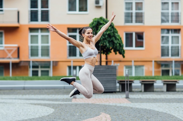 Fit laufende junge Athletin fliegt durch die Luft, während das Laufen eine Schnur in der Luft macht, die einen Lauf in einer Stadt macht.