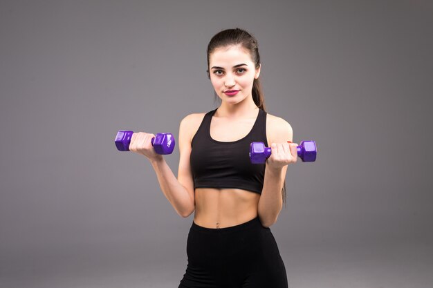 Fitness junge Frau mit Hanteln auf einer grauen Wand. Sportlicher Lebensstil.