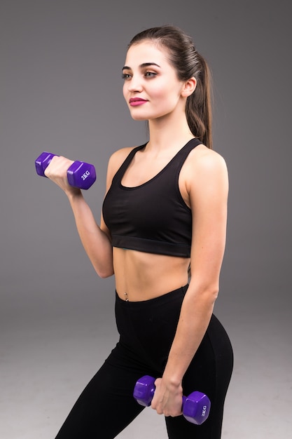 Fitness junge Frau mit Hanteln auf einer grauen Wand. Sportlicher Lebensstil.