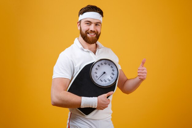 Fitness-Mann, der Gewichtswaagen hält und Daumen hoch zeigt