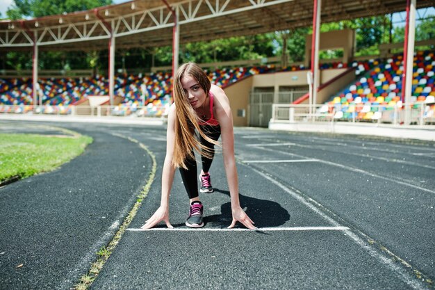 Fitness sportliches Mädchen in Sportbekleidung im Stadion im Freien Sport Glückliche sexy Frau, die auf dem Laufband der Leichtathletikbahn im Stadion läuft