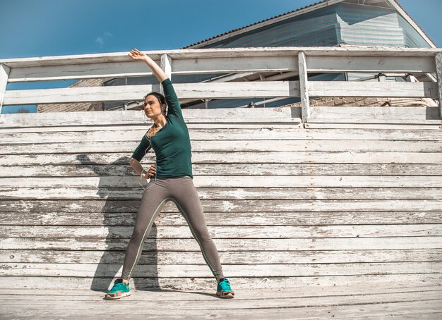 Fitness sportliches Mädchen in sportlicher Kleidung macht Übungen auf einem hölzernen Hintergrund, hellem Hintergrund, dem Konzept des Sports