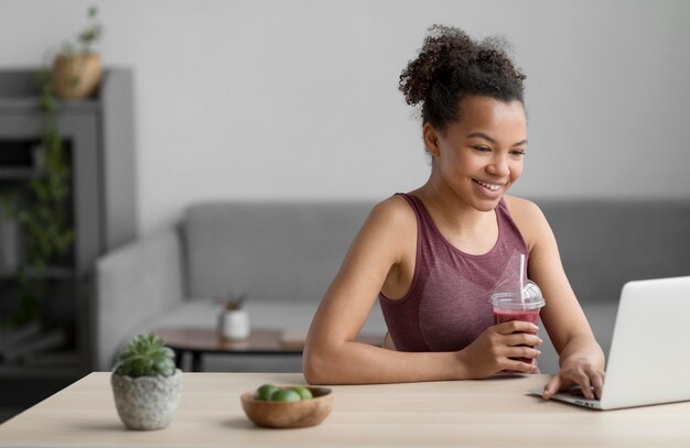 Fitnessfrau, die einen Fruchtsaft beim Verwenden eines Laptops hat