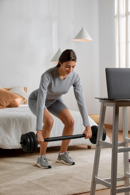 Fitnesstrainerin beim Heben von Gewichten zu Hause vor dem Laptop