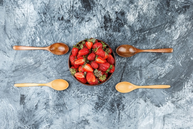 Flach eine Schüssel Erdbeeren mit Holzlöffeln auf dunkelblaue Marmoroberfläche legen. horizontal