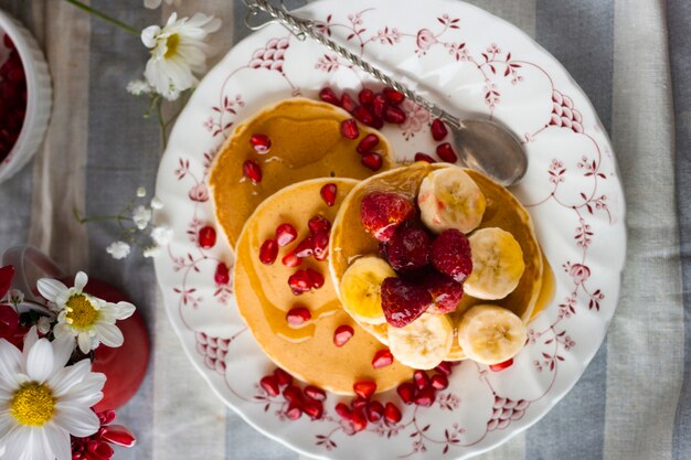 Flach gelegte Pfannkuchen mit Granatapfelkernen, Bananen und Himbeeren