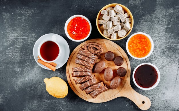 Flach geschnittene Roulade in Schneidebrett und Schalen mit Tee, Waffeln und Gelee auf Dunkelheit legen