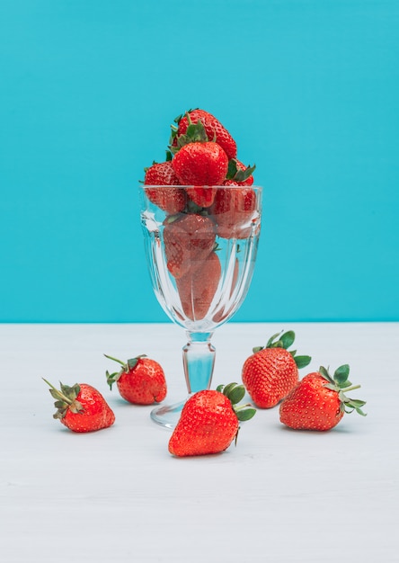 Flach lag Bündel Erdbeeren im Glas mit mehreren um dieses auf blauem Hintergrund. horizontal