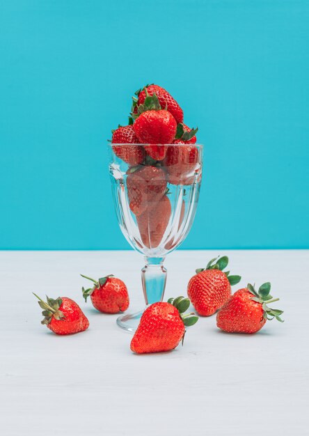 Flach lag Bündel Erdbeeren im Glas mit mehreren um dieses auf blauem Hintergrund. horizontal