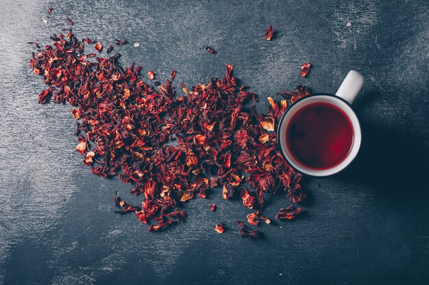 Flach lag eine Tasse Tee mit Teekräutern auf dunklem strukturiertem Hintergrund. horizontal