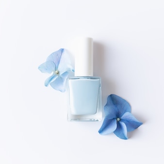 Flach mit hortensia blauen blütenblättern mit blauem nagellack in einer transparenten glasflasche liegen. natürliches maniküre- und pediküre-konzept