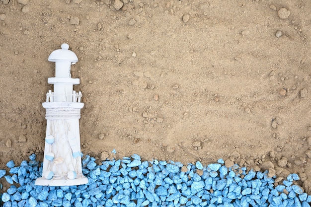 Flache blaue kieselsteine mit leuchtturm auf sand legen