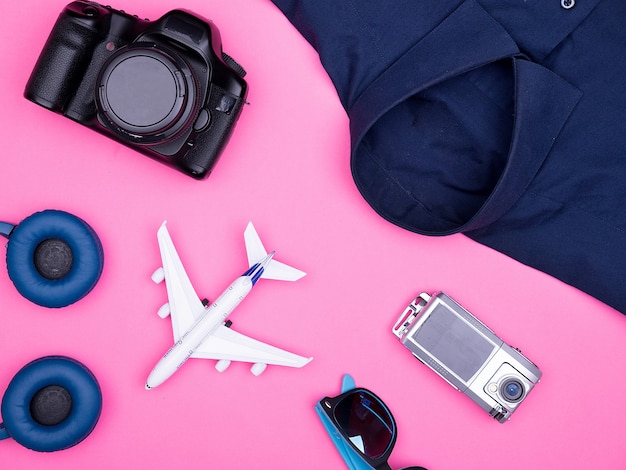 Flache Draufsicht auf das Zubehör von Reisendenfotografen auf rosafarbenem Hintergrund. Kamera, Sonnenbrille. Kopfhörer. Shirt