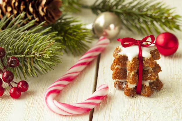 Flache Fokus-Nahaufnahmeaufnahme eines Ingwerplätzchens neben einer Zuckerstange und Weihnachtsbaumzweigen