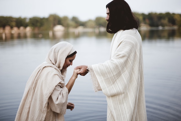 Flache fokusaufnahme einer frau, die ein biblisches gewand trägt, während sie die hand jesu christi hält holding