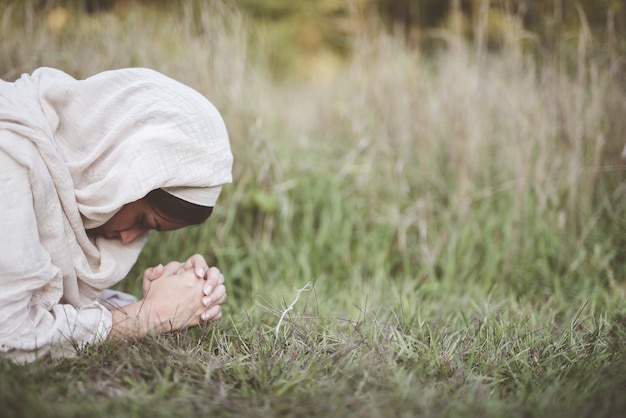 Flache Fokusaufnahme einer Frau unten auf dem Boden, die betet, während sie ein biblisches Gewand trägt