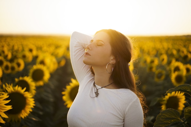 Kostenloses Foto flache fokusaufnahme einer hübschen europäischen frau in einem sonnenblumenfeld bei sonnenaufgang