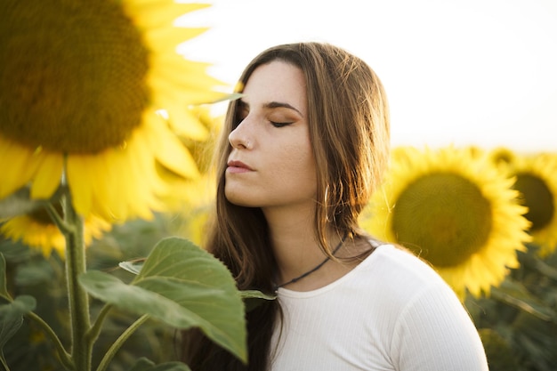 Flache fokusaufnahme einer hübschen europäischen frau in einem sonnenblumenfeld bei sonnenaufgang