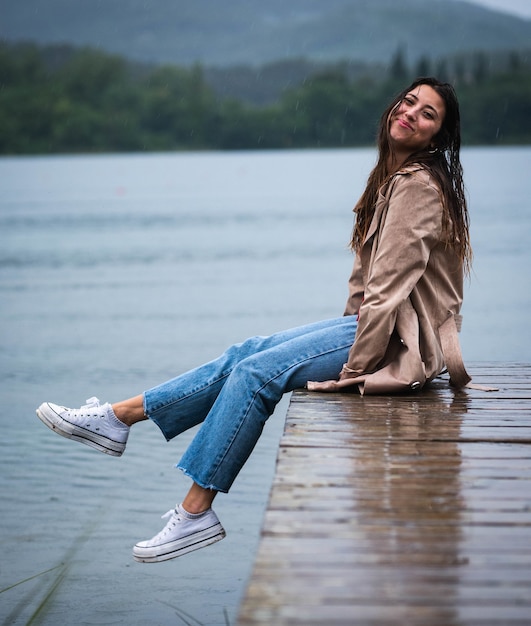 Flache Fokusaufnahme einer jungen Frau, die im Regen auf einem Holzsteg sitzt