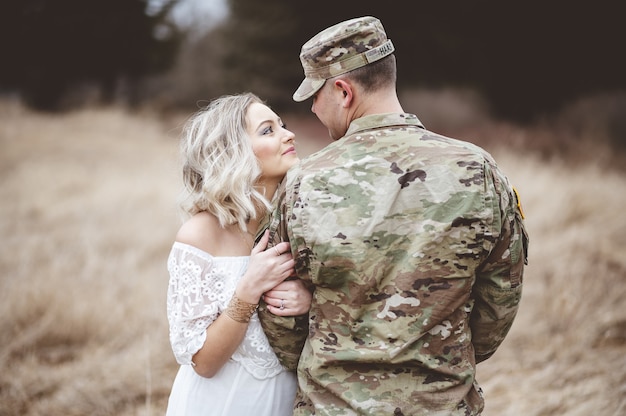 Flache Fokusaufnahme eines amerikanischen Soldaten mit seiner liebenden Frau, die auf einem Feld steht