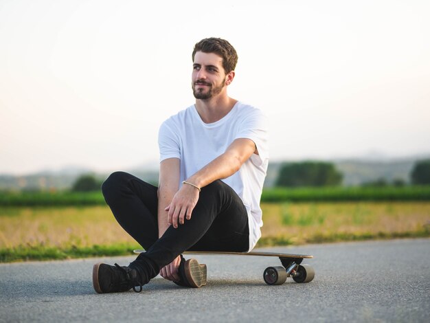 Flache Fokusaufnahme eines jungen gutaussehenden Mannes, der auf einem Skateboard sitzt