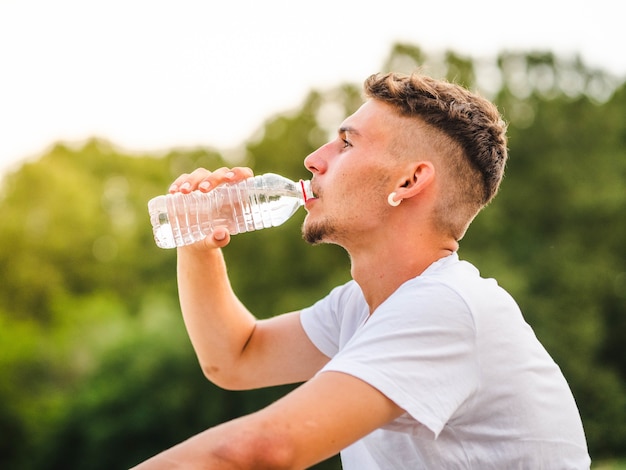 Flache Fokusaufnahme eines kaukasischen männlichen Trinkwassers nach einem Training in einem Park