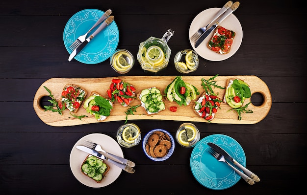 Flache Lage der gesunden vegetarischen Tischdekoration. Sandwiches mit Tomaten, Gurken, Avocado, Erdbeere, Kräutern und Oliven, Snacks. Sauberes Essen, veganes Essen