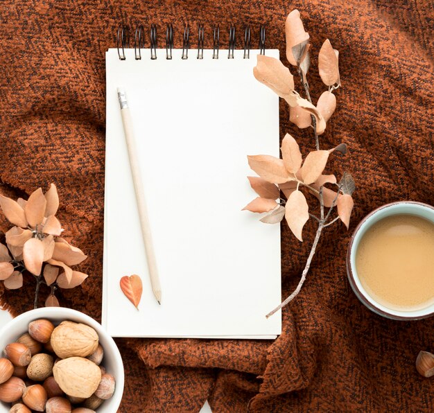 Flache Lage der Kaffeetasse mit Herbstlaub und Notizbuch