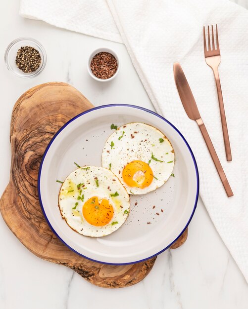 Flache Lage der Spiegeleier des Frühstücks auf Teller mit Besteck