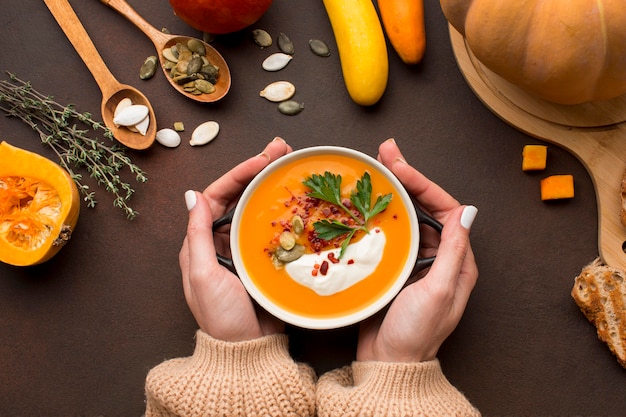 Flache Lage der Winterkürbissuppe in der Schüssel, die von Händen gehalten wird