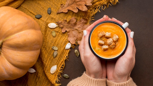 Flache Lage der Winterkürbissuppe mit Croutons im Becher, der von Händen gehalten wird