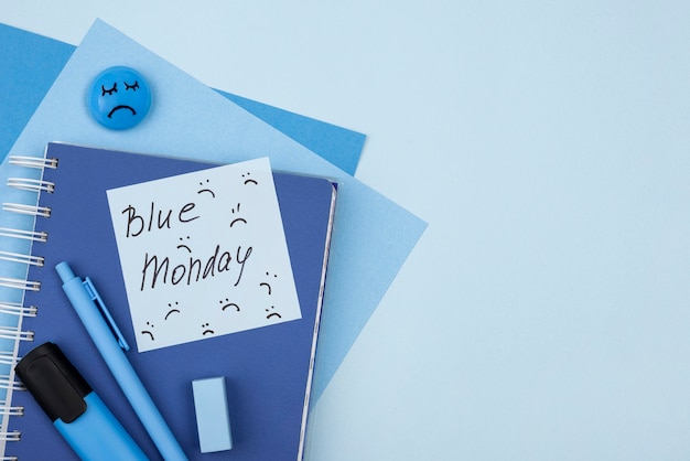 Flache Lage des traurigen Gesichts des blauen Montags mit Notizbuch und Marker