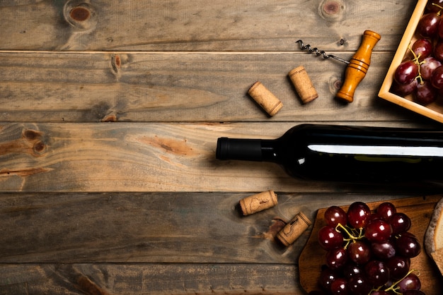 Flache Lage einer Flasche Wein, umgeben von Korken und roten Trauben