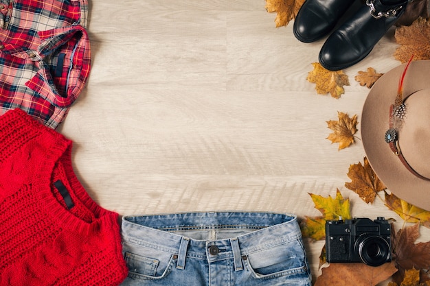 Flache Lage von Frauenstil und Accessoires, roter Strickpullover, kariertes Hemd, Jeans, schwarze Lederstiefel, Hut, Herbstmode-Trend, Blick von oben, Vintage-Fotokamera, Traveller-Outfit