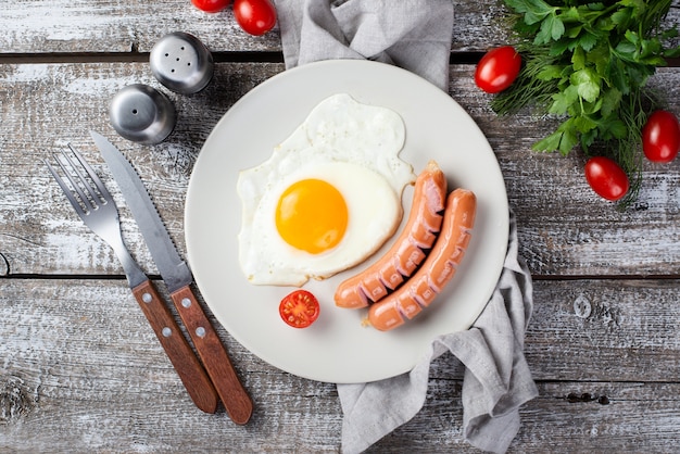Flache Lage von Frühstückswürsten und -ei auf Platte mit Tomaten und Tischbesteck