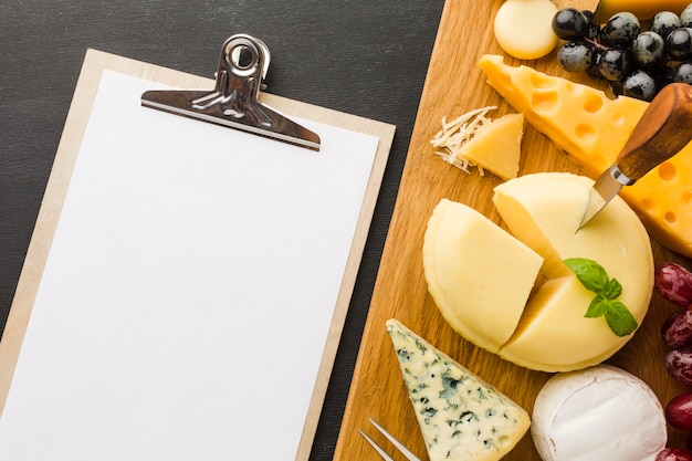 Kostenloses Foto flache laienmischung des feinschmeckerischen käses und der trauben auf schneidebrett mit leerem notizbuch