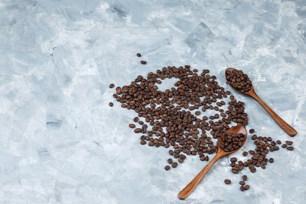 Flache legen Kaffeebohnen in Holzlöffeln auf grauem Gipshintergrund. horizontal