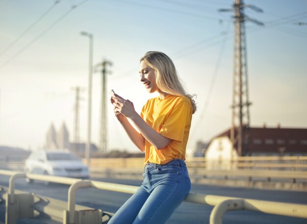 Flacher Fokus einer aufgeregten Frau, die sich an einen Brückenzaun lehnt und eine SMS auf ihr Telefon schreibt