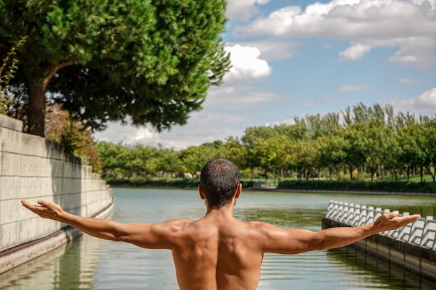 Flacher Fokus eines Mannes, der in einem Teich meditiert, umgeben von Grün unter dem Sonnenlicht