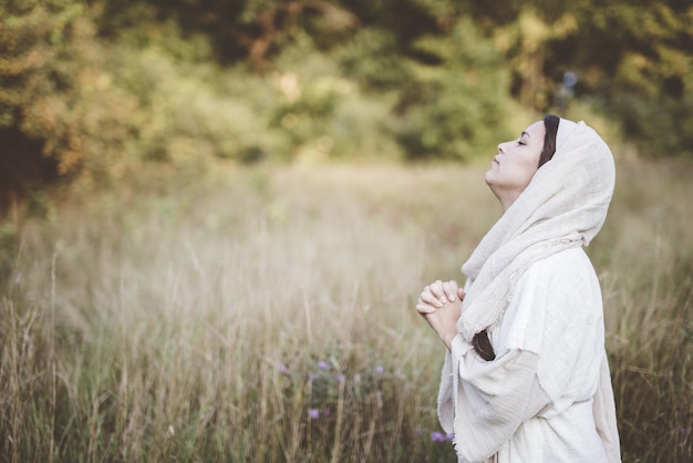 Flacher Fokusschuss der Frau, die eine biblische Robe trägt, die mit ihrem Kopf in Richtung Himmel betet