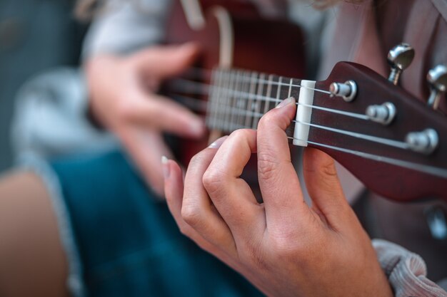 Flacher Fokusschuss einer Person, die Jeans trägt, während sie ein Lied auf der Ukulele spielt