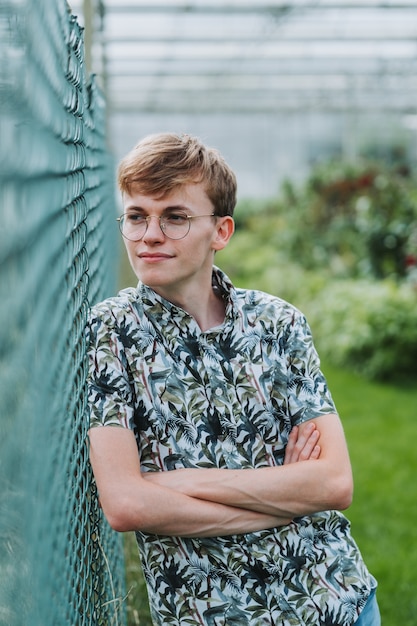 Kostenloses Foto flacher fokusschuss eines jungen mannes mit brille, die sich auf einen zaun stützt