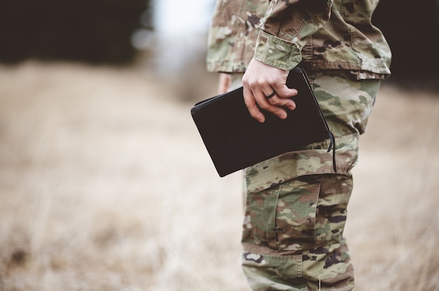 Flacher Fokusschuss eines jungen Soldaten, der eine Bibel in einem Feld hält