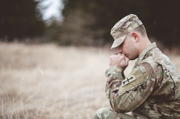 Flacher Fokusschuss eines jungen Soldaten, der in einem Feld betet